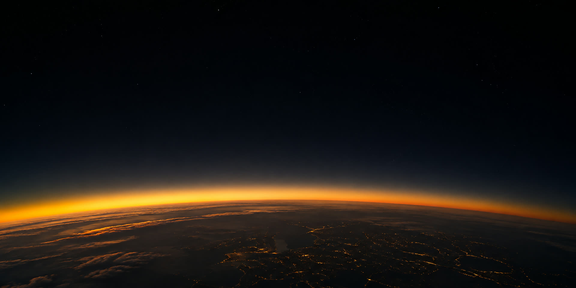 Earth's curved horizon seen from high altitude at the day and night line, a band of gold atmosphere glowing along the curve above scattered city lights